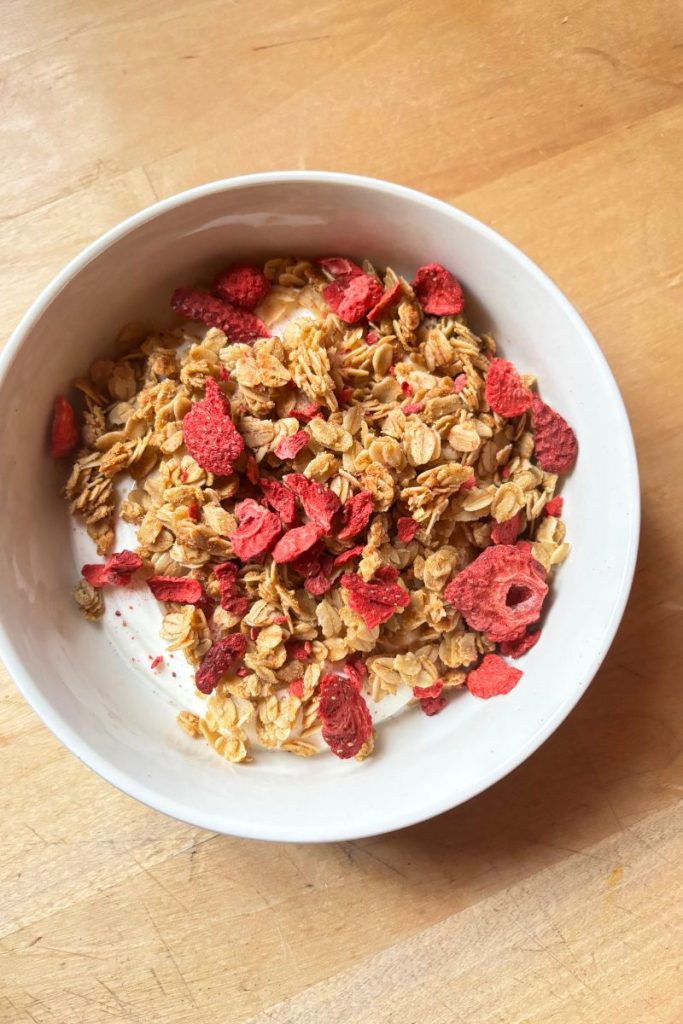 White bowl of greek yogurt, granola and freeze dried strawberries