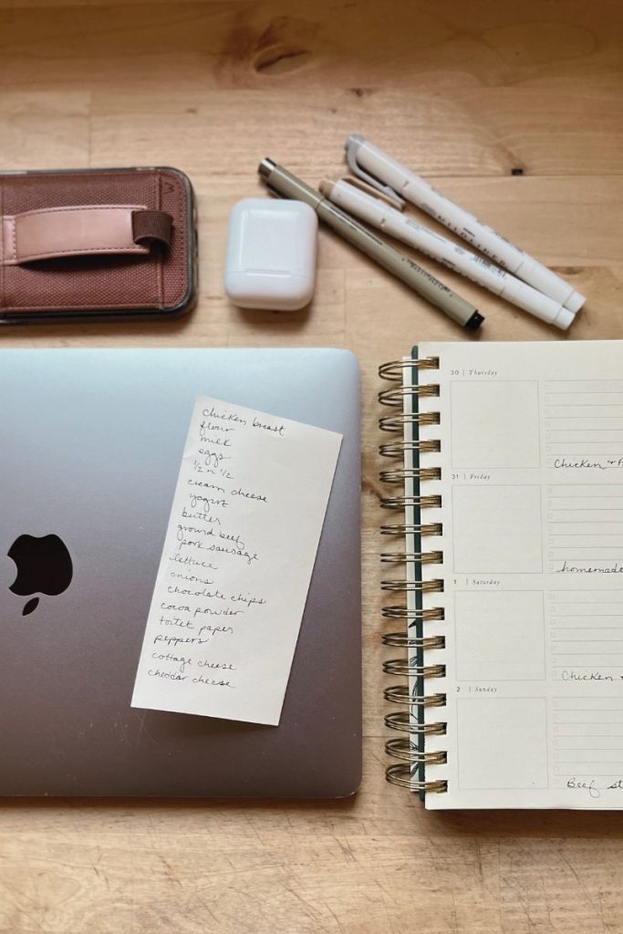 Items for meal planning - Countertop with phone, MacBook, pens, AirPod case, and planner