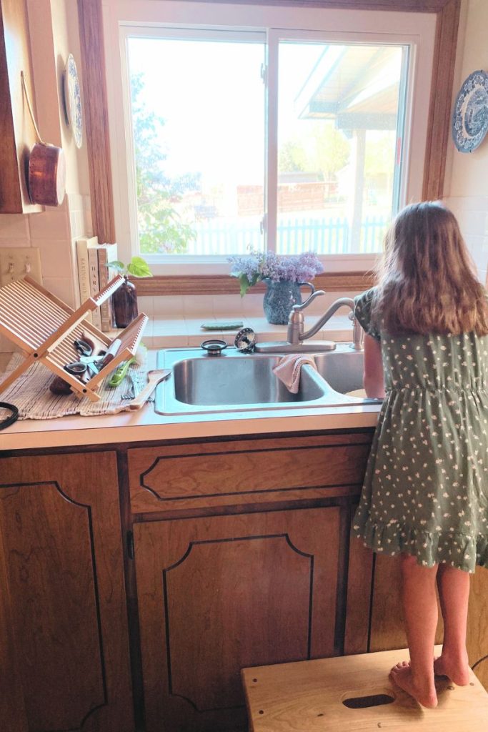 young girl washing dishes at a sink with window